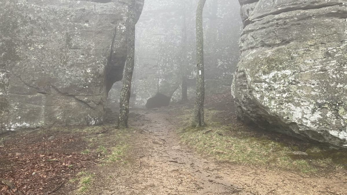 Hiking trail with bluffs on either side and a cave.
