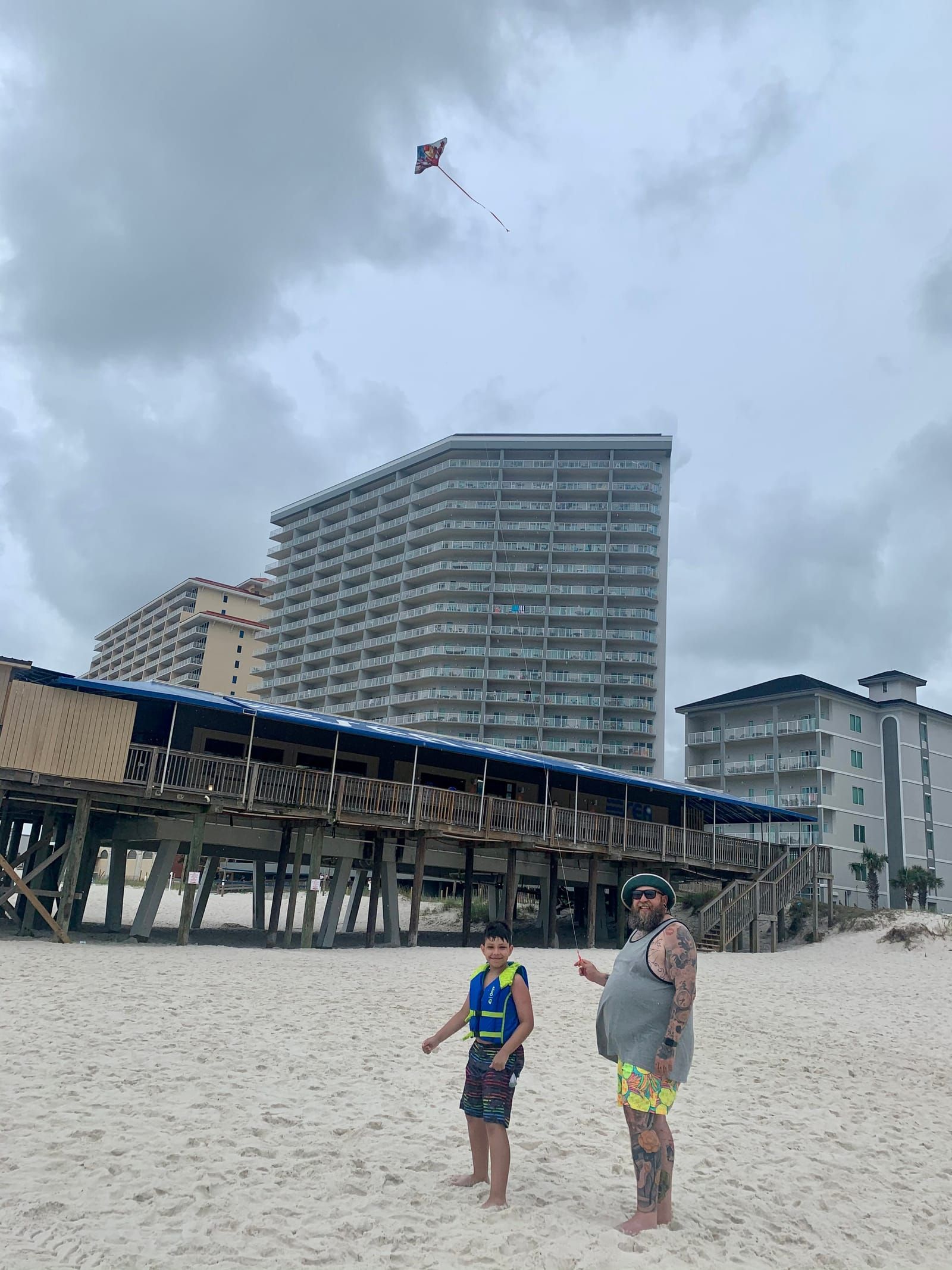 10 year old Carter and Papa Mike flying a kite on the beach with hotels in the background.