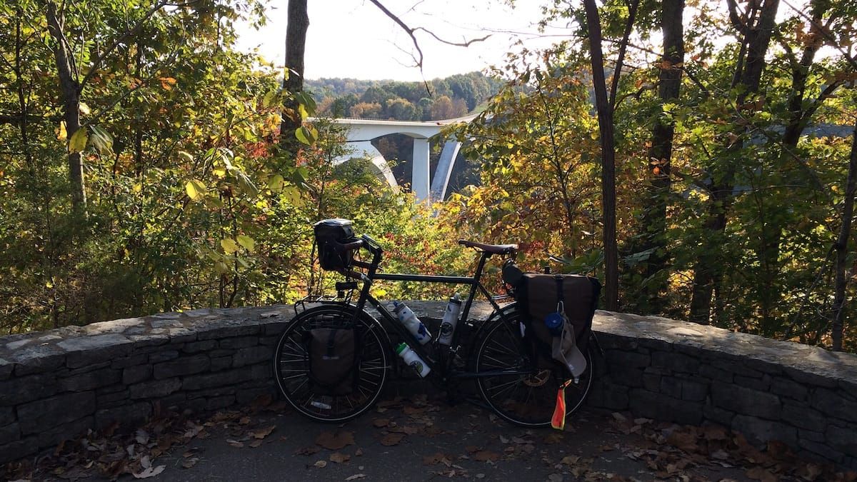 Touring bicycle leaning against a low stone wall with the bridge in the background.