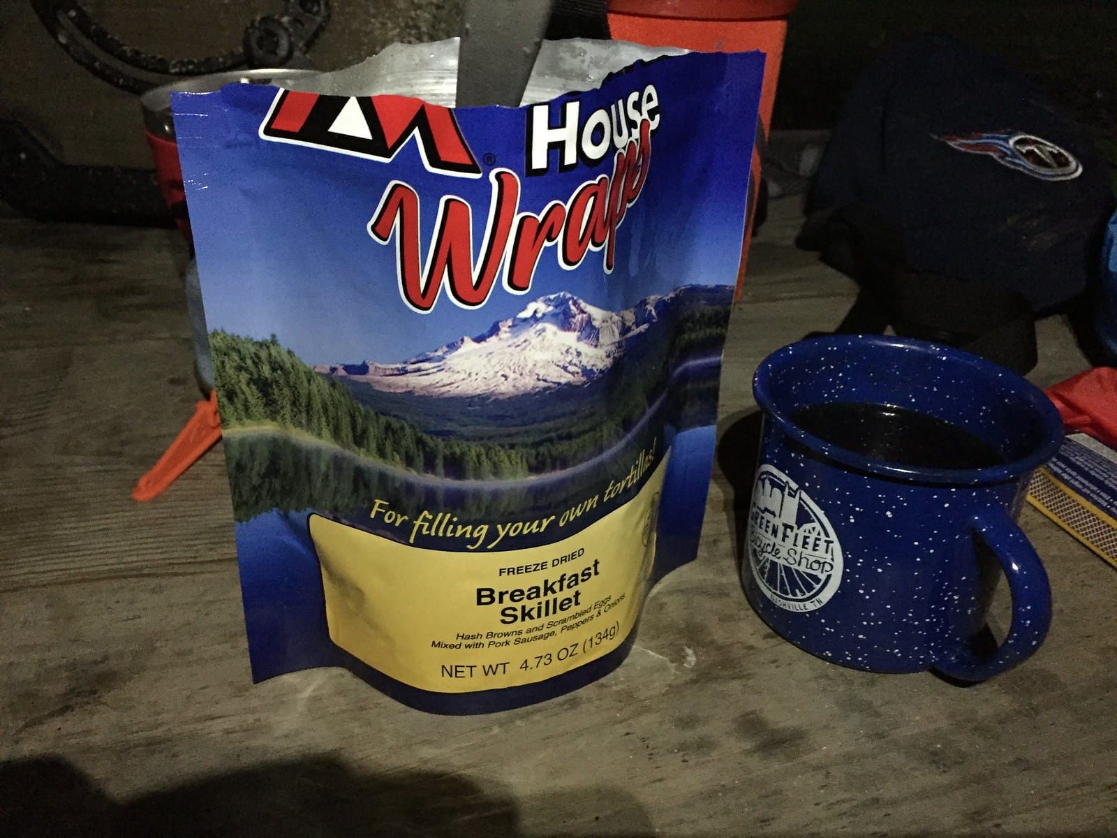 Opened Mountain House freeze dried breakfast skillet meal with a blue camp cup of coffee.