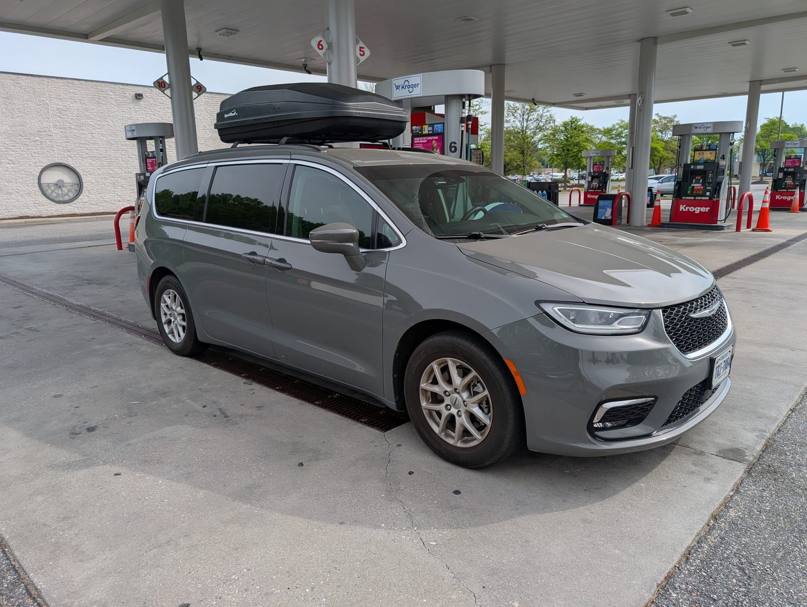 A dirty gray van sits at a gas station. A roof rack storage container is up top