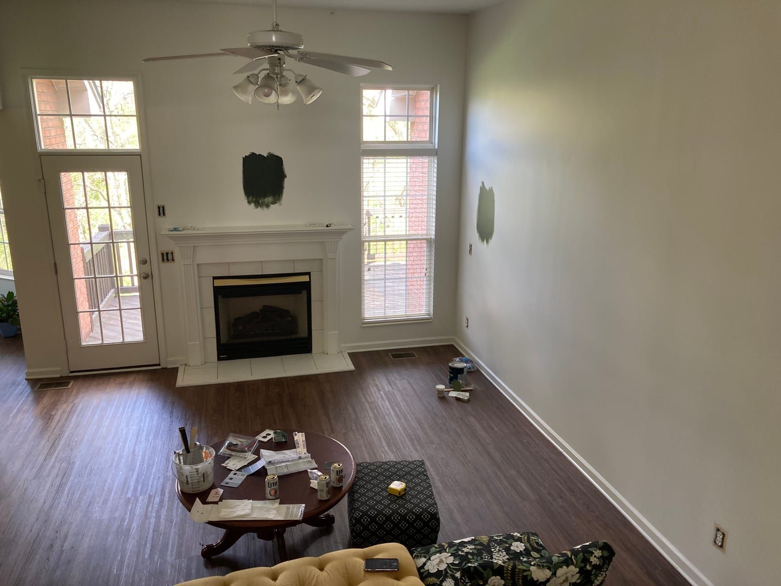 The empty living room of the new house. Test green paint patches are painted on two walls. A coffee table with some painting equipment and beer cans are in the foreground.