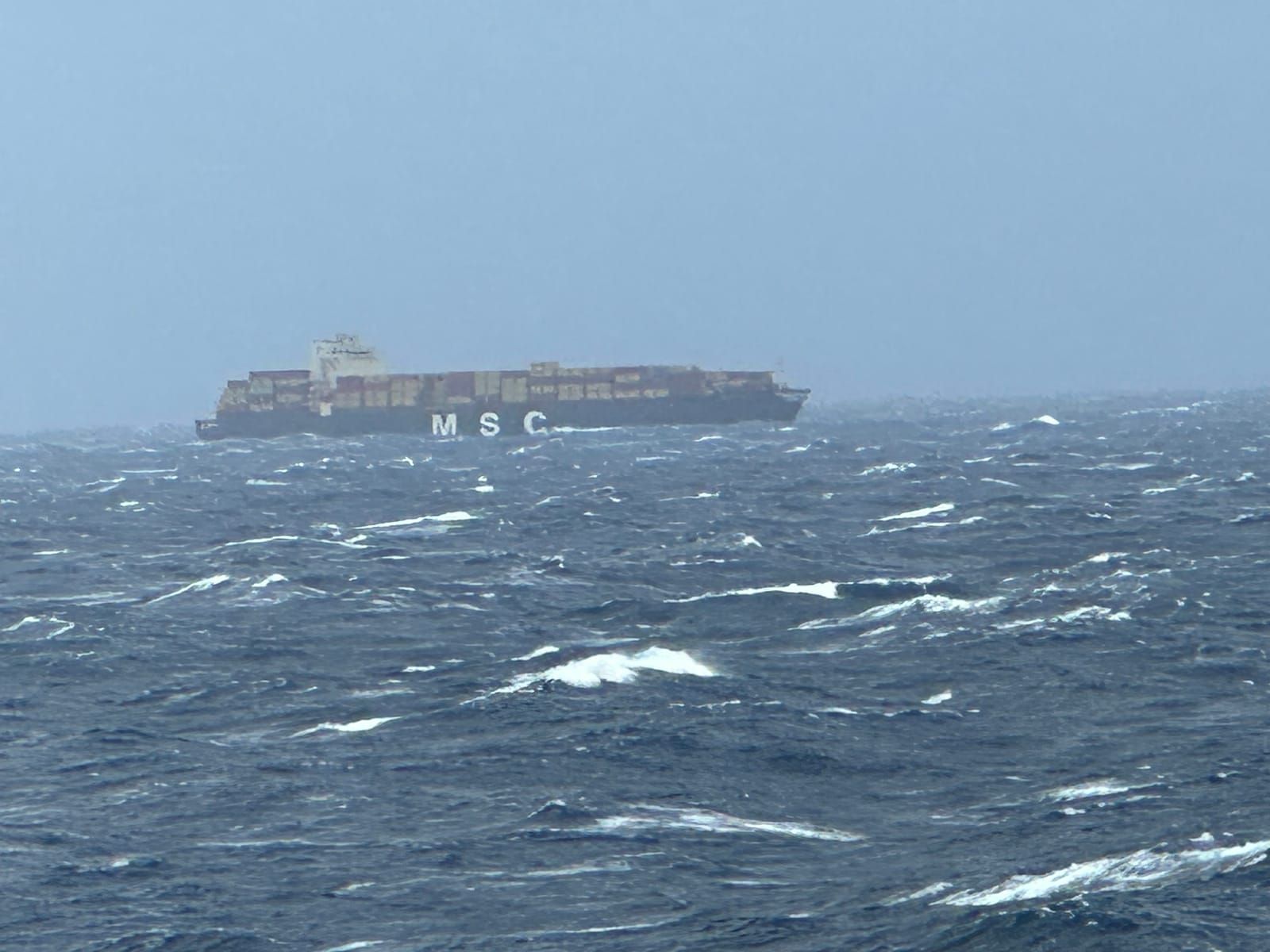 A freighter in the distance with rough seas in the foregrouna and an overcast sky.