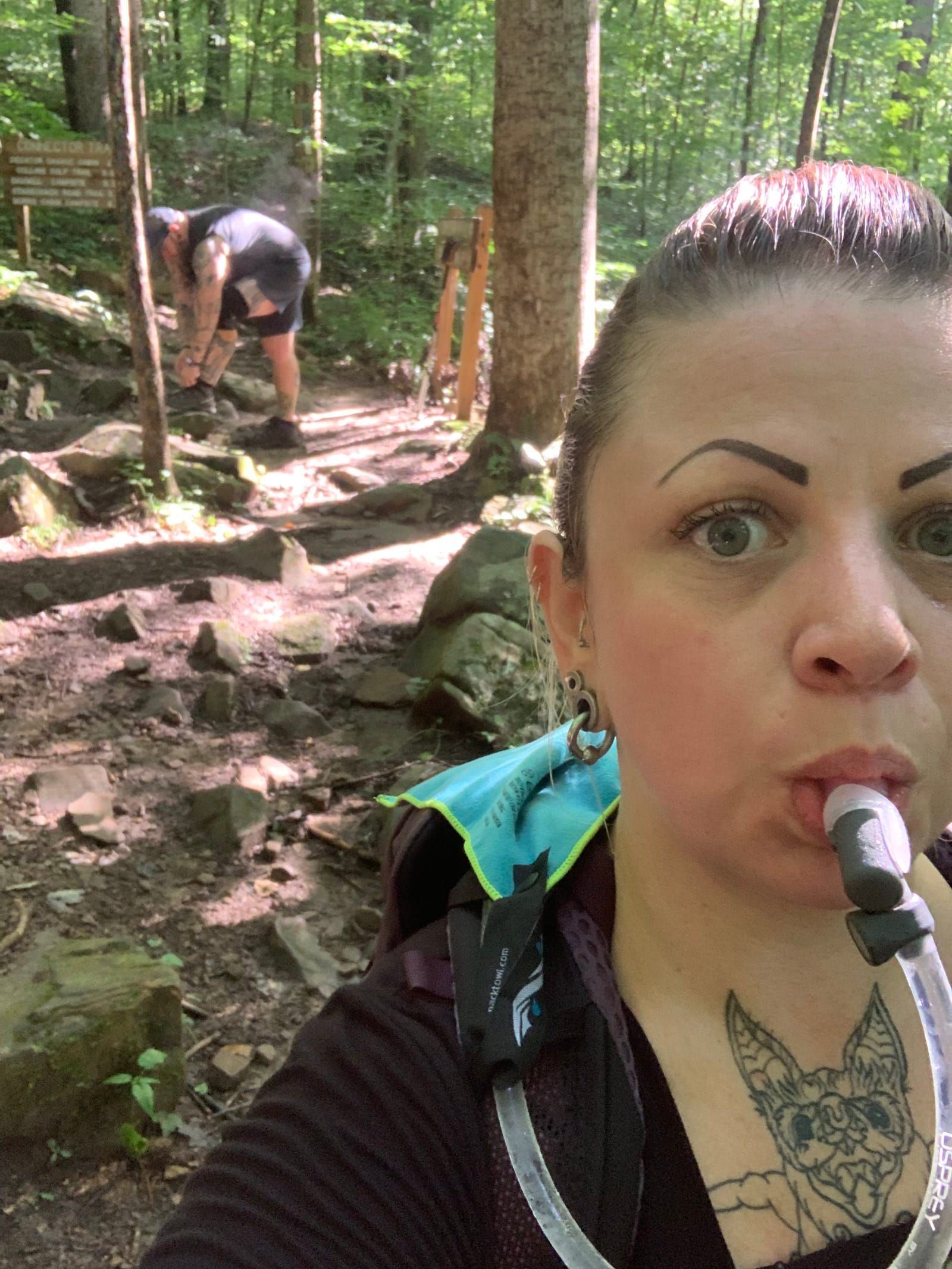 Meredith drinking water from her camel back with Mike bending over in the background tying his shoe with steam coming off his back because it's so humid.