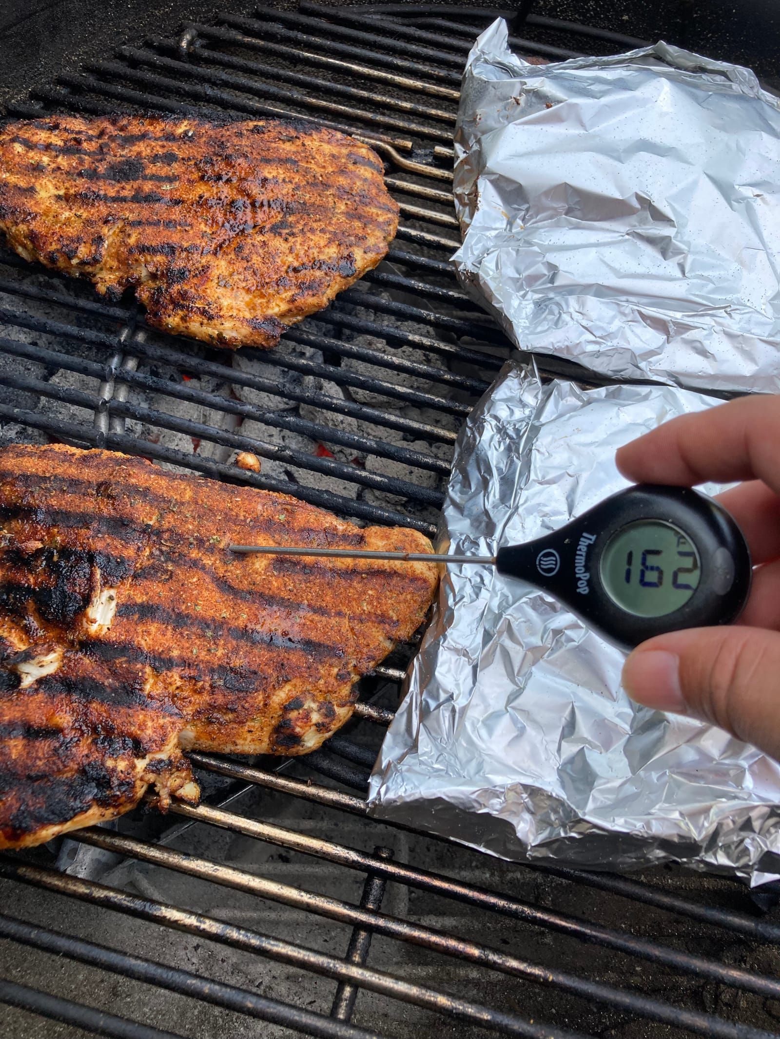Grilled chicken breast on the grill with a therometer stuck into one of the, the screen reads 162.