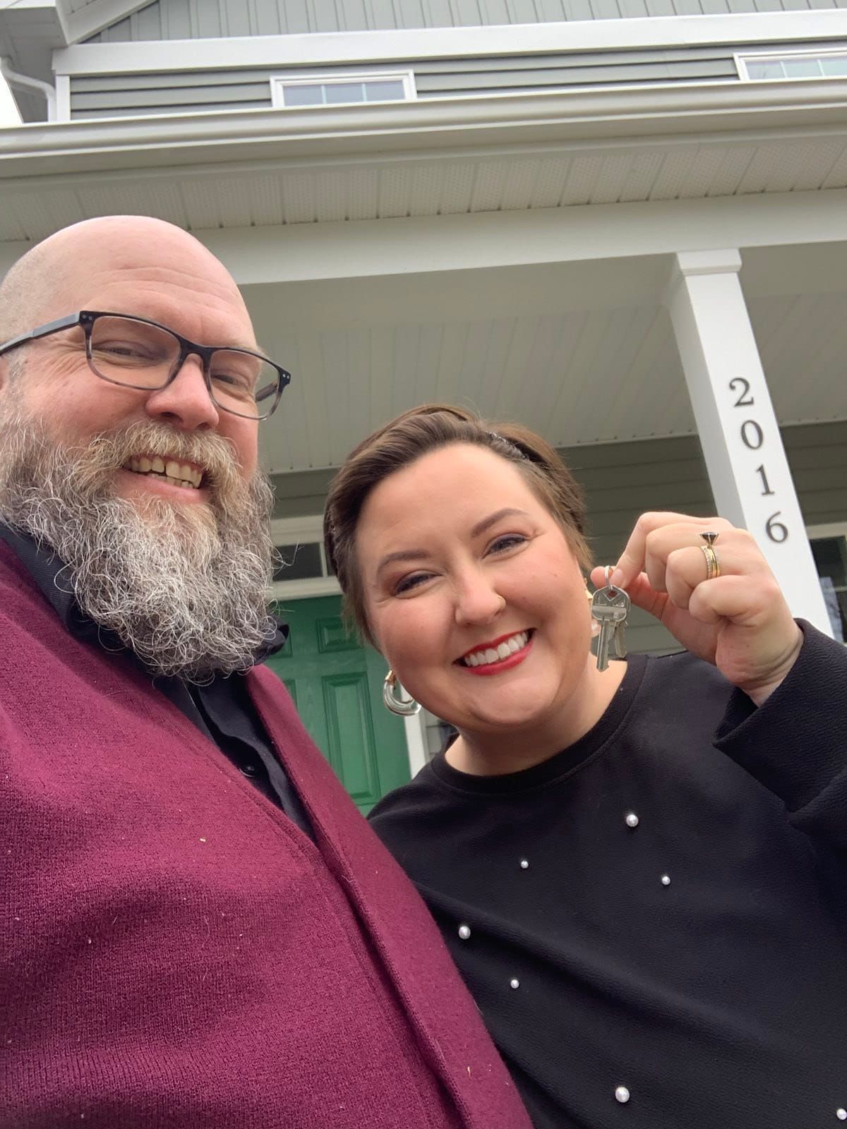 Mike and Rachelle posing for a selfie in front of their new house holding the keys to the new house.