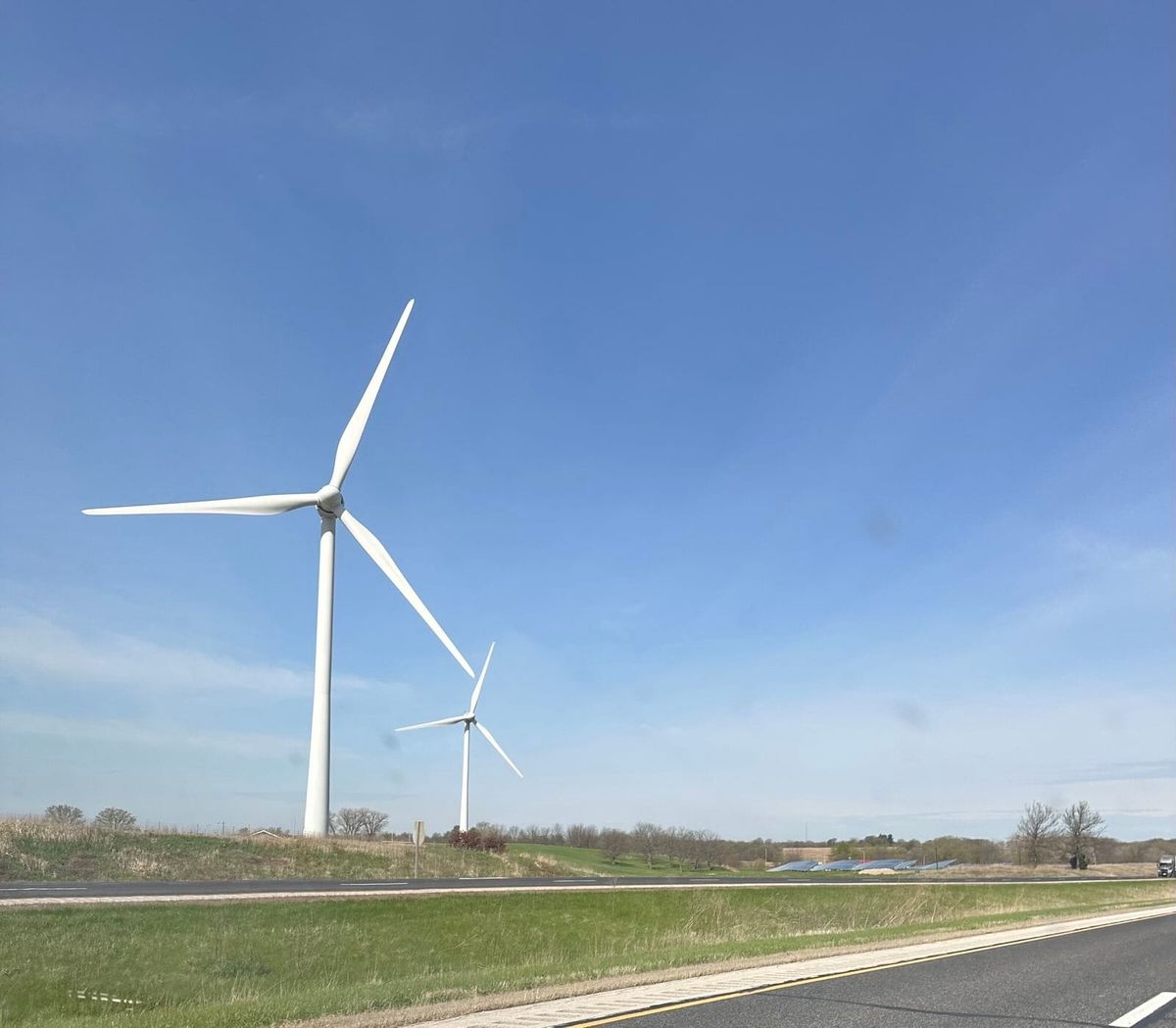 Photo from the van as we travel down the interstate. Two large windmills are visible and a crystal clear blue sky.