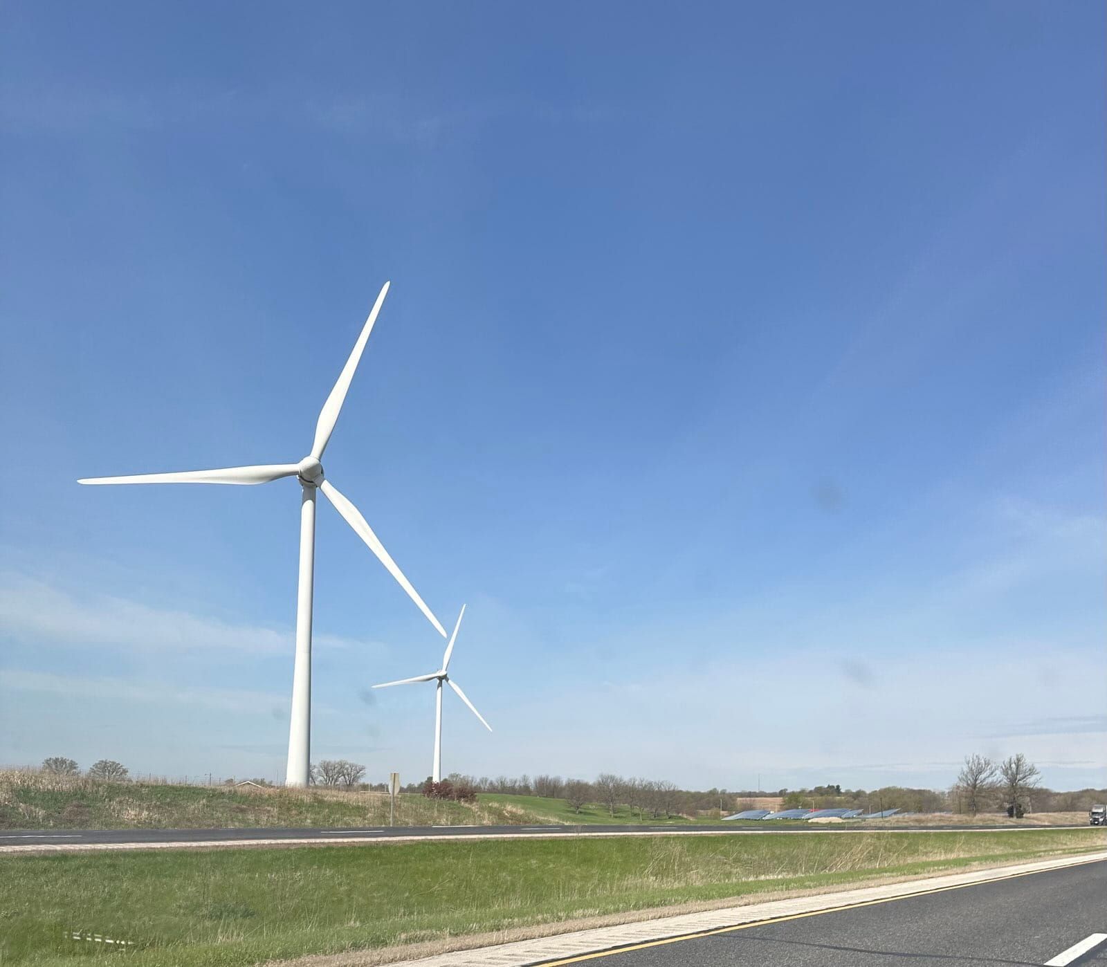 Photo from the van as we travel down the interstate. Two large windmills are visible and a crystal clear blue sky.
