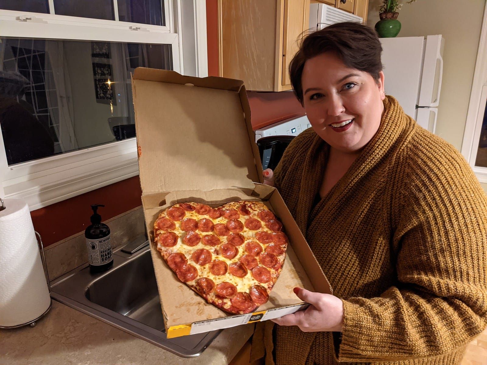 Rachelle looking at the camera, holding a heart shaped pizza.