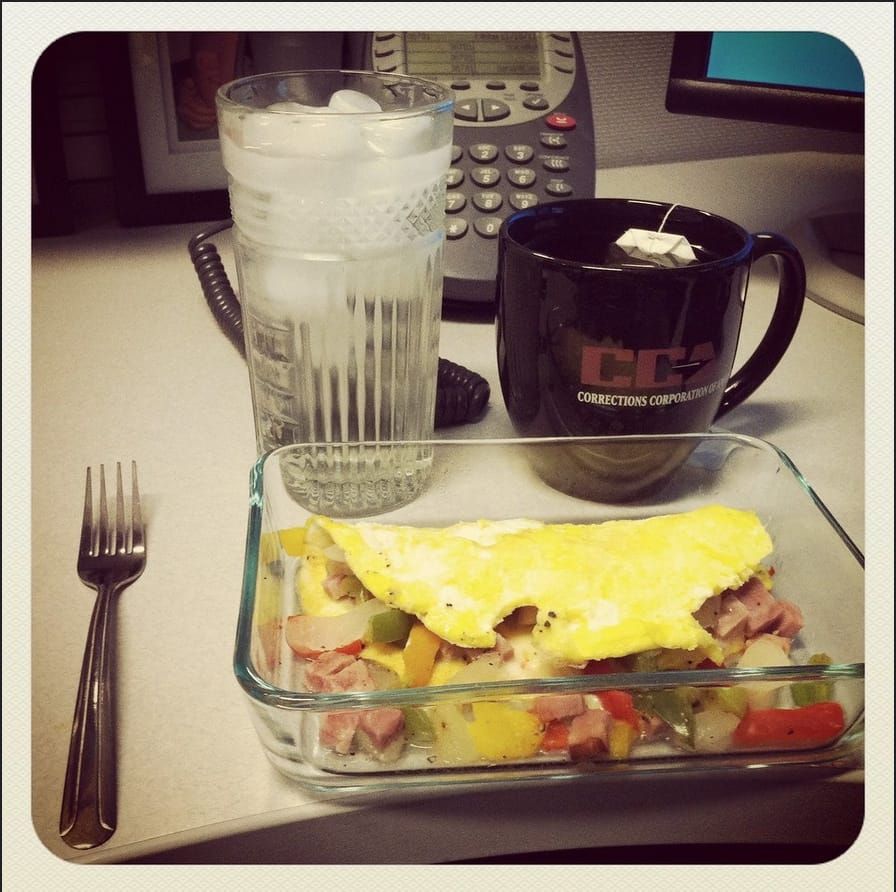 Omelet in a pyrex dish, on work desk with water and tea on the side.