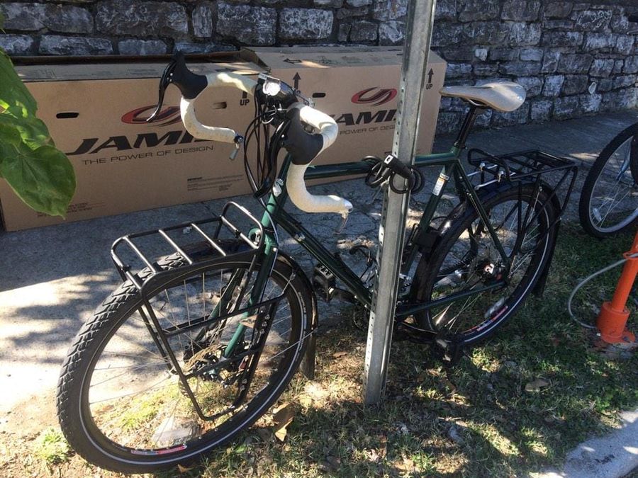Tank bicycle standing next to a sign post. Forest green bicycle with tan seat and handlebar tape.