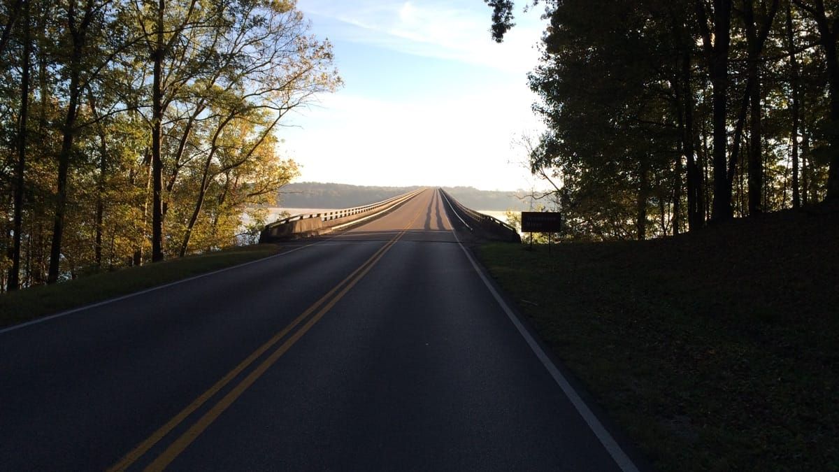 Approach to the bridge, with the morning shade giving way to sun light as the road crosses the river.