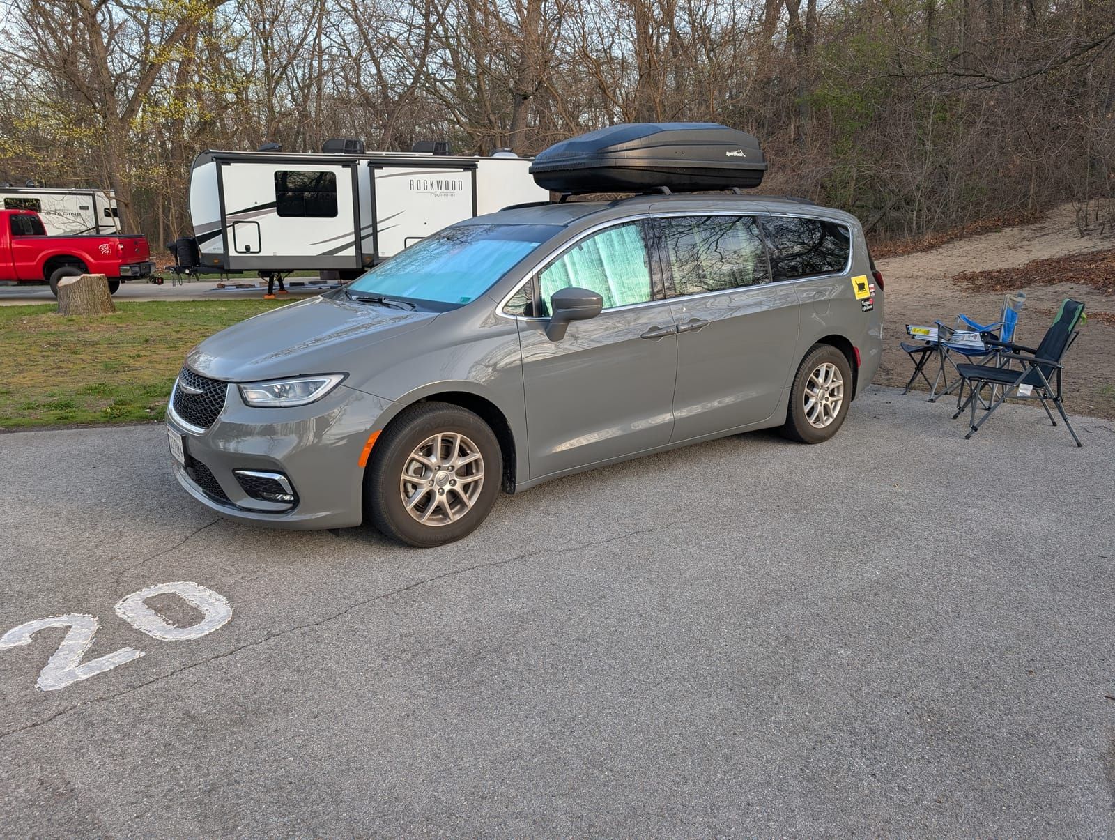 Minivan backed into a car camping spot. Sun screens are in the window and camp chairs are setup.