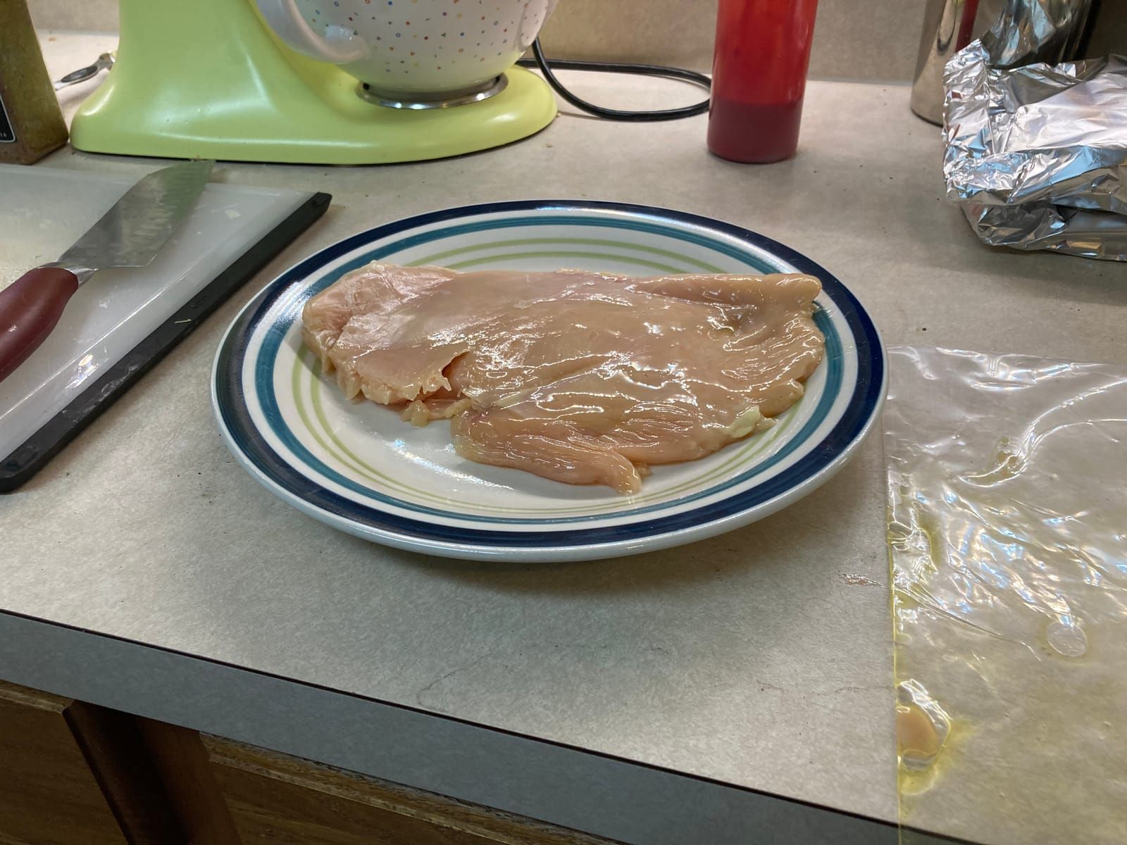 The flattened chicken breast, on a plate after beating it with the rolling pin.