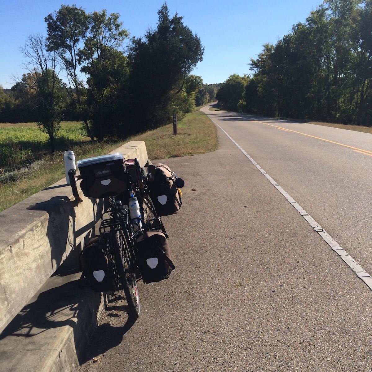 Loaded touring bicycle leaning against a bridge over pass, from the front.