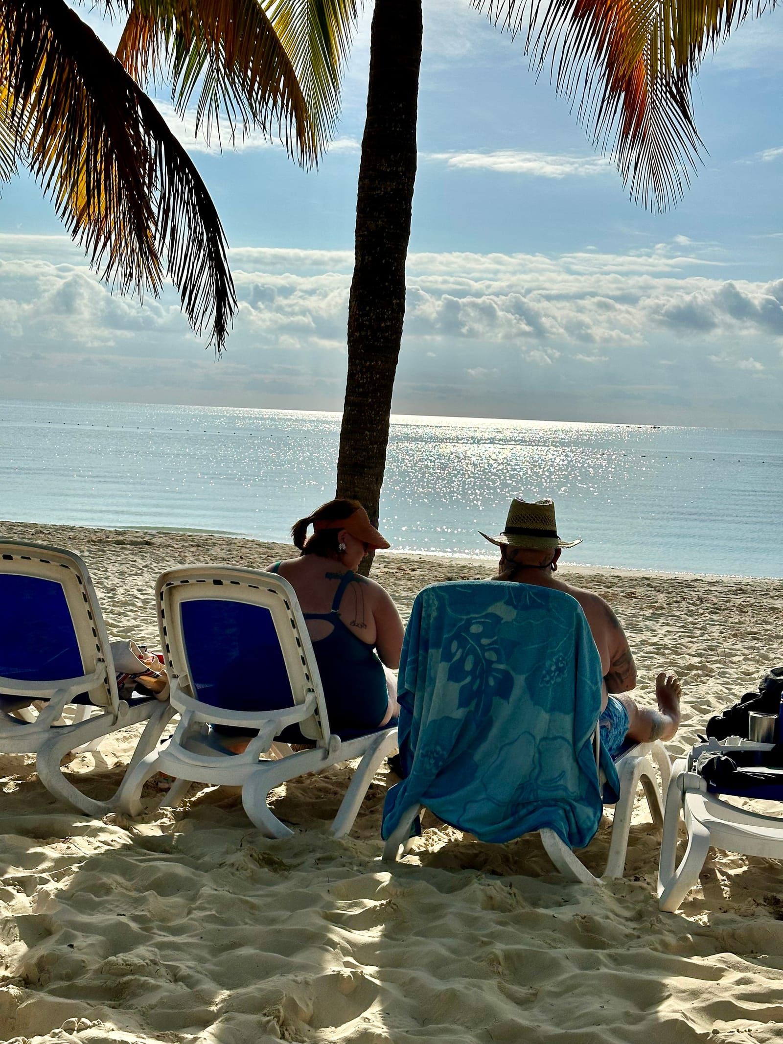 Photo of Michael and Rachelle sitting in beach chairs at the beach, under palm trees.