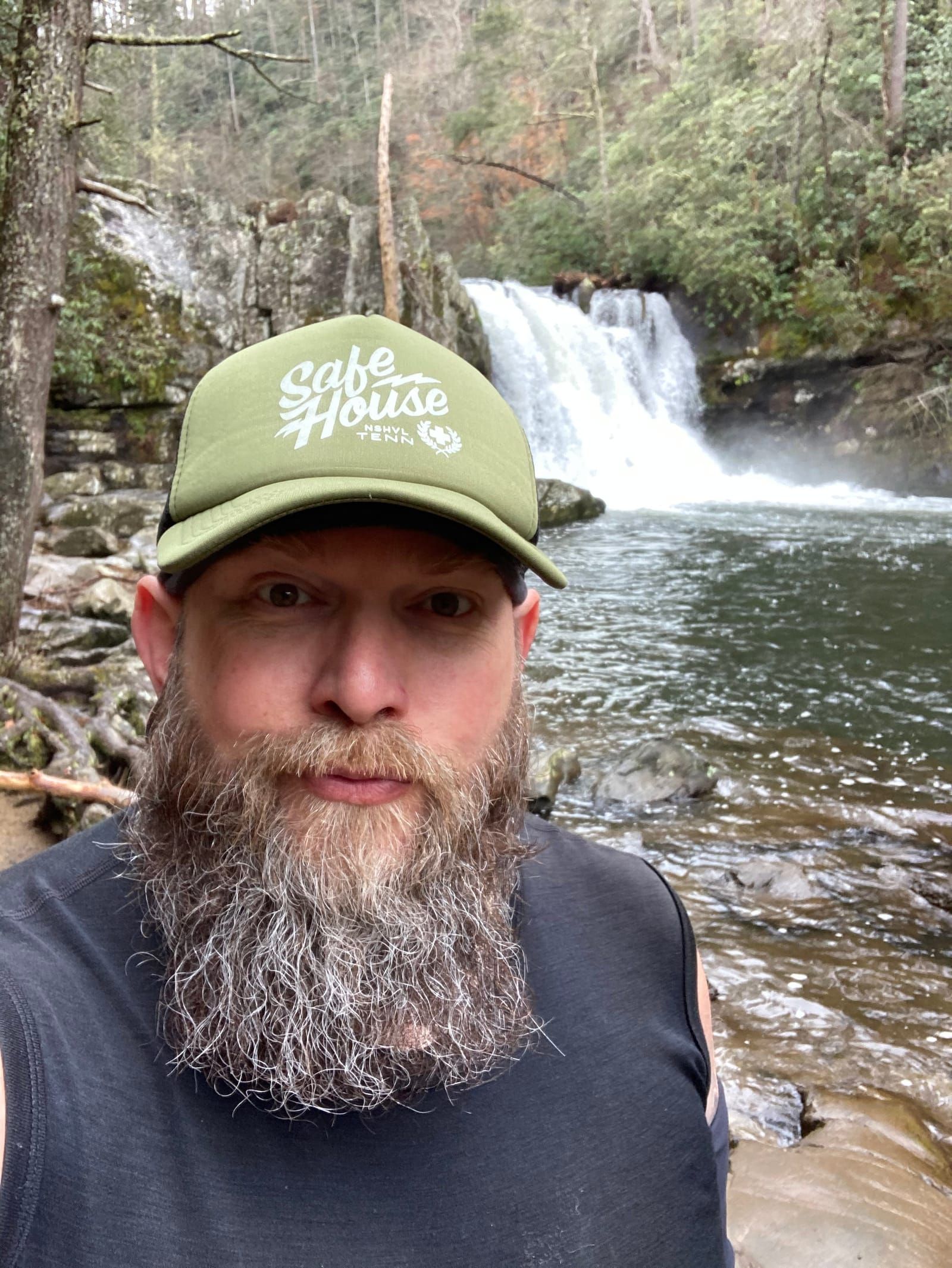 Bearded Mike wearing a green Safe House tattoo hat takes a photo in front of Abrams Falls.