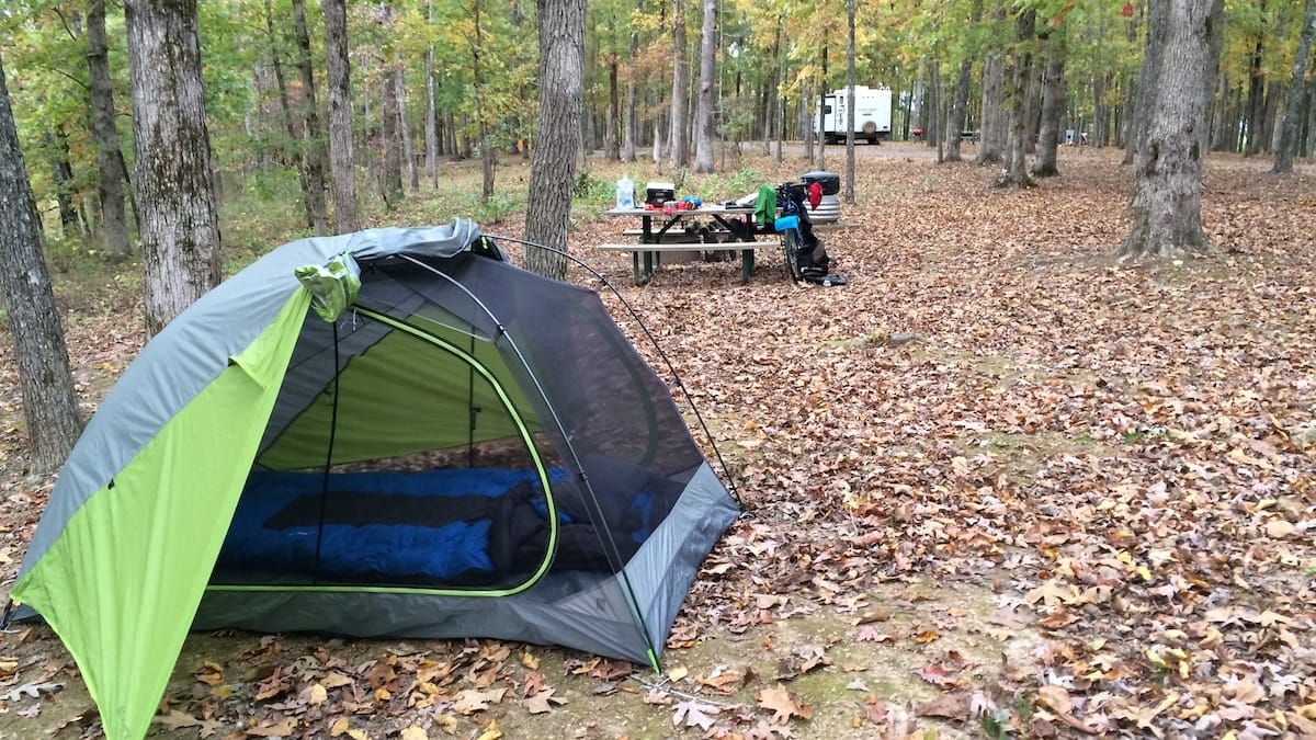 Evening camp site with tent in the foreground and bicycle propped against a picnic table in the background.