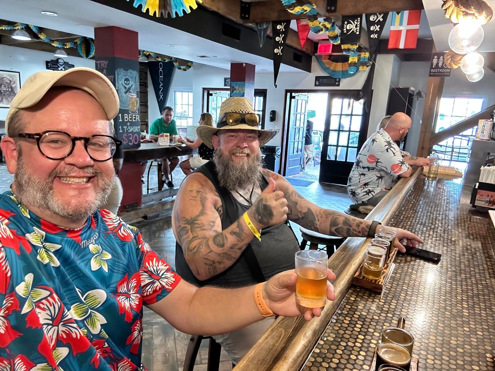 Smiling selfie of Kevin and Michael. Kevin holds a flight glass of beer. Michael is giving a big thumbs up.