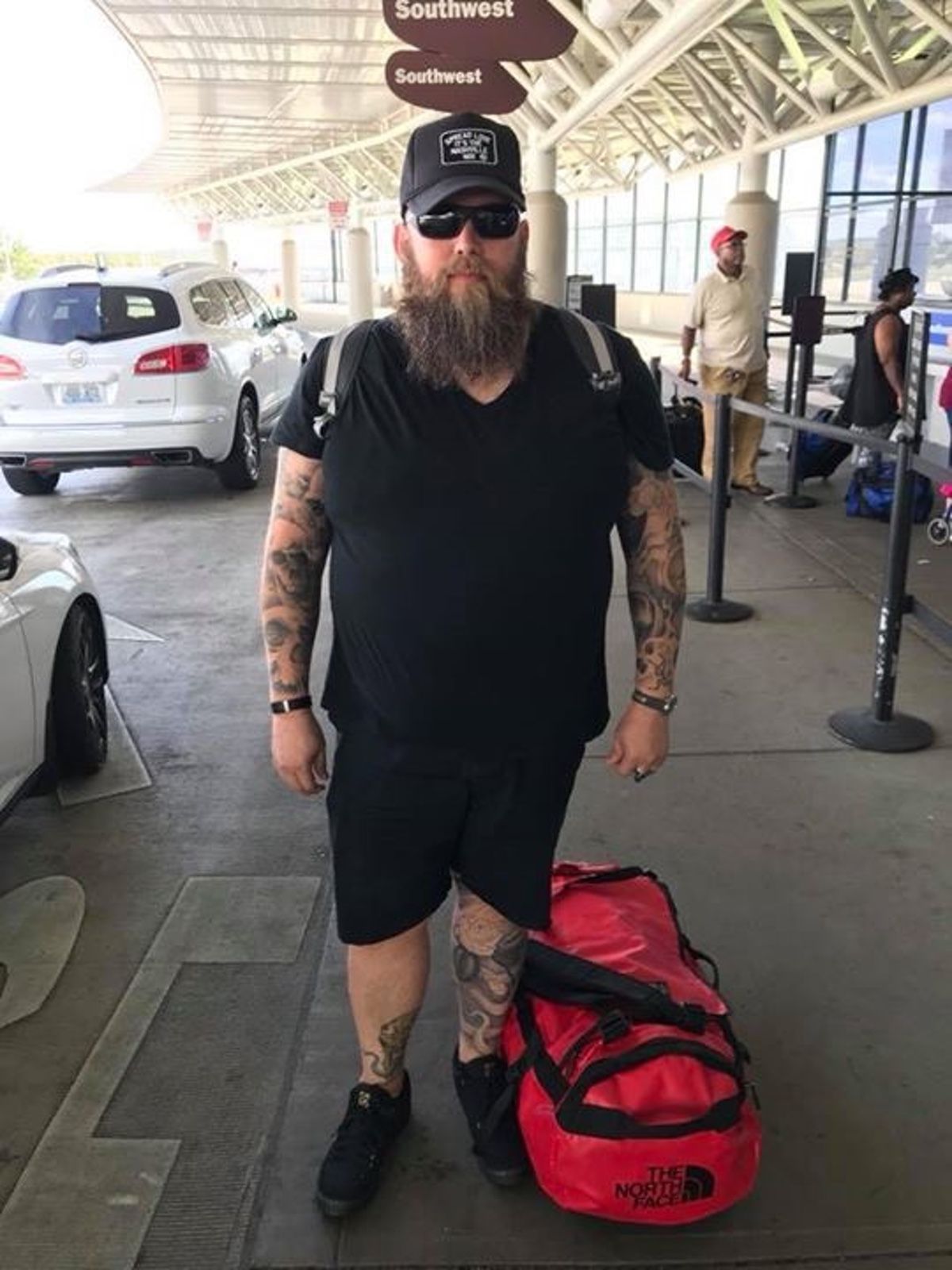 Mike standing with his bag packs, sun glasses and hat at the Nashville airport.