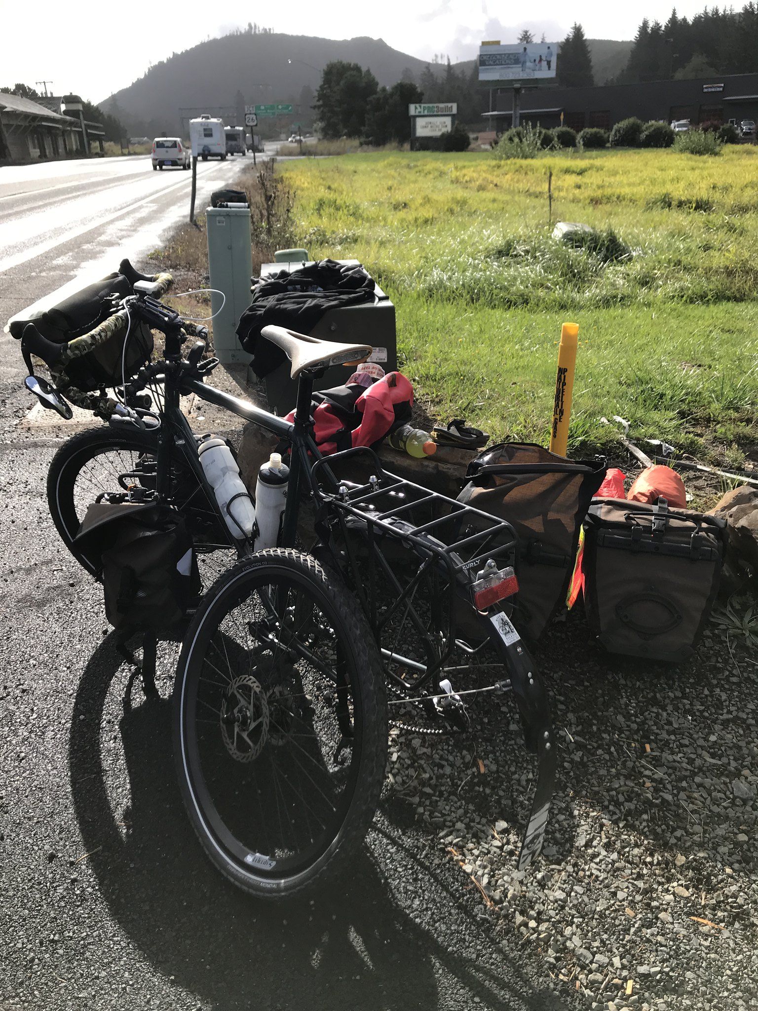 Tank bicycle on the side of the road with the back wheel off and panniers unloaded.