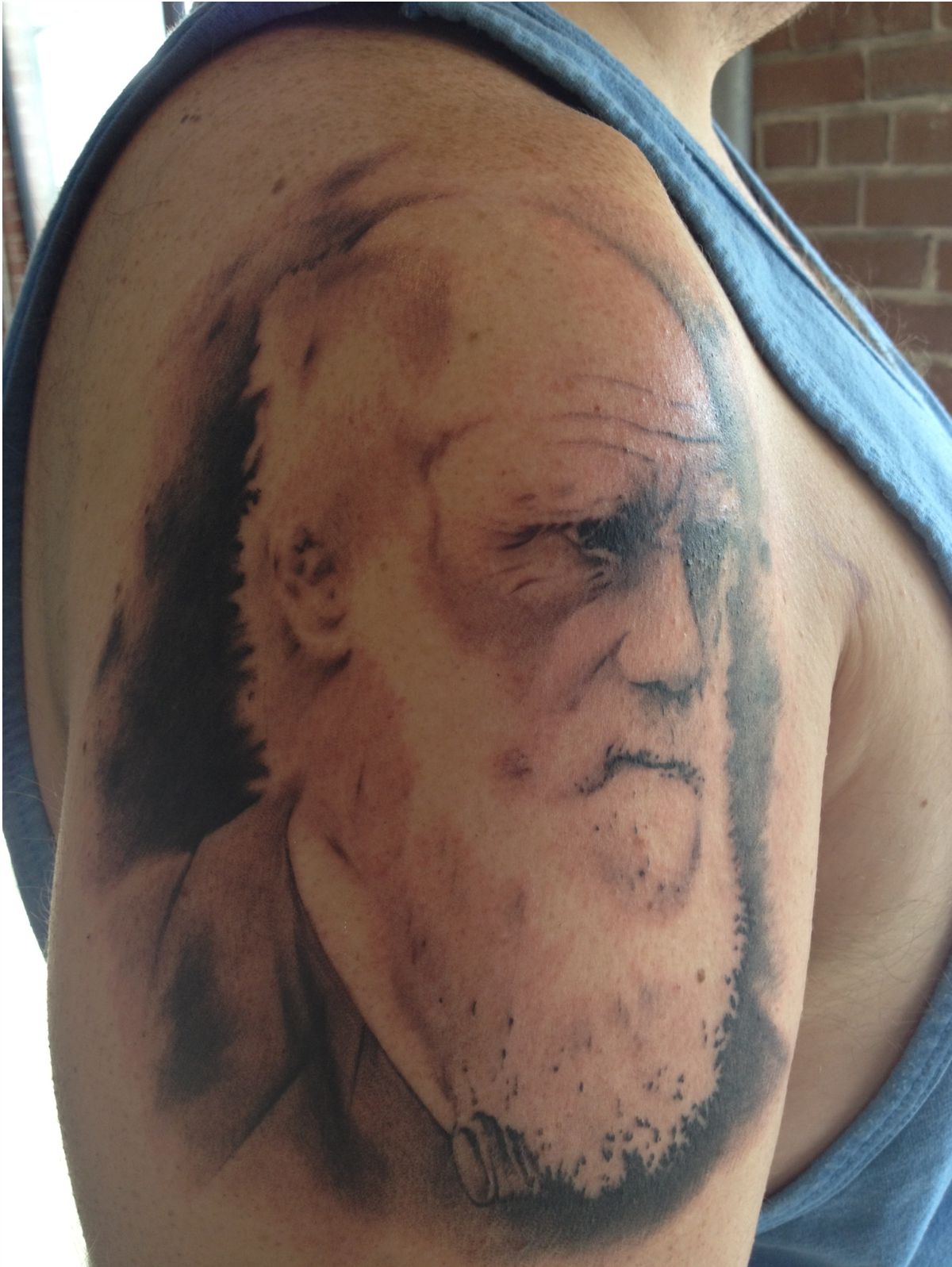 Black and gray portrait tattoo of the famous Charles Darwin photo.