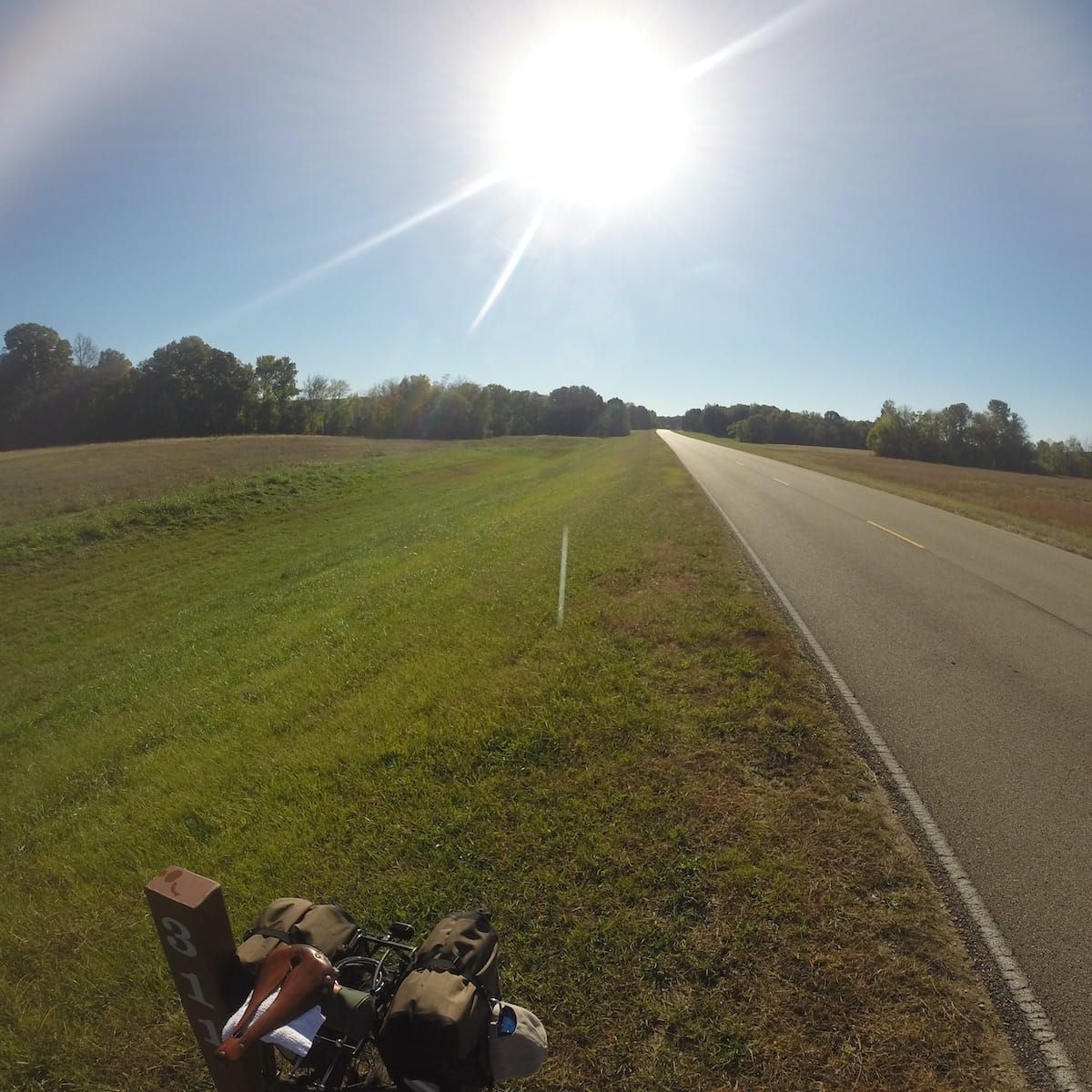 Partial view of touring bicycle leaning against mile marker 311, looking backwards. Bright sun shine. 