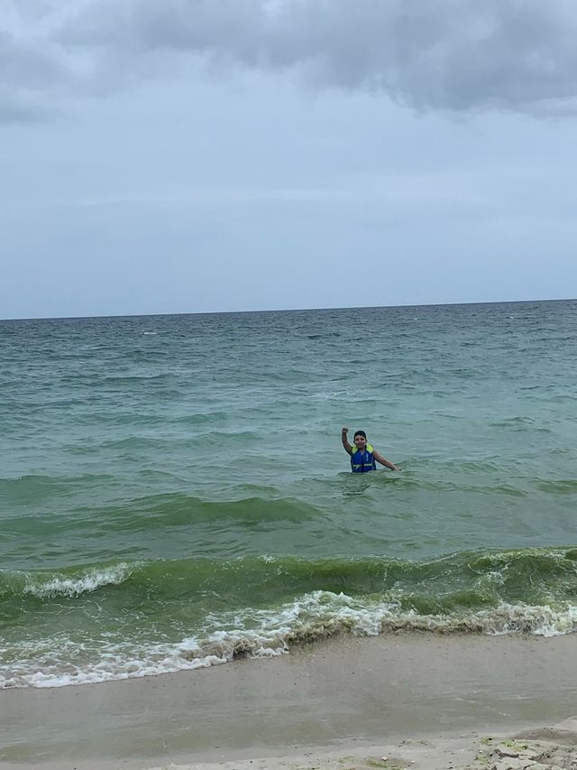 10 year old Carter in the ocean wearing a life vest and waving from the water towards the camera.