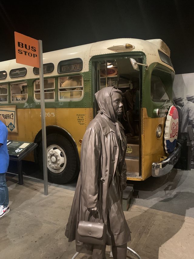 Museum display of a 50s era bus and the bus boycott in Birmingham. Statue of a black woman walking instead of riding the bus is portrayed in the foreground.