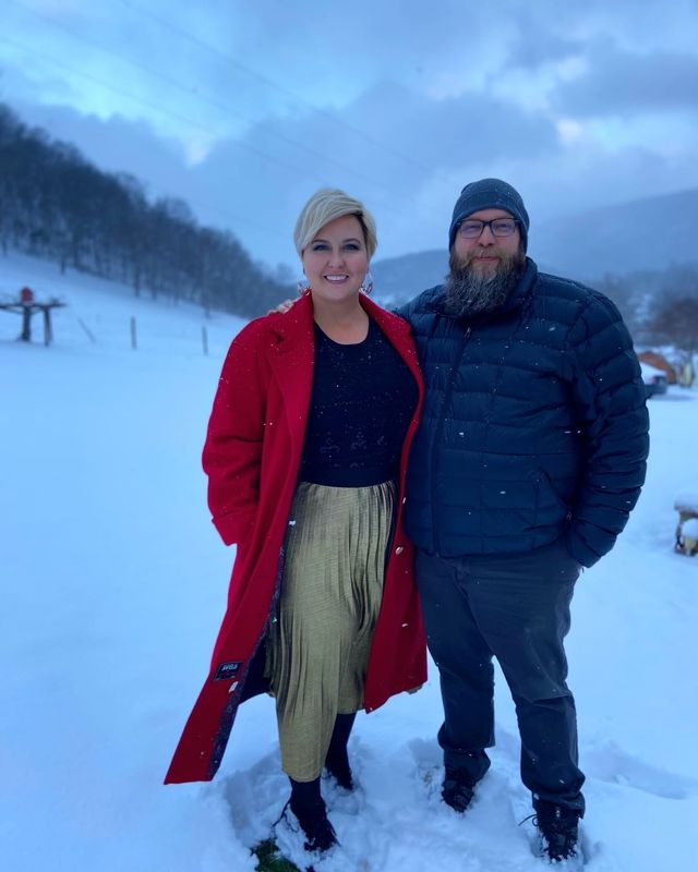 Mike and rachelle in the snow. Rachelle wearing a vivid red coat on a snowy, overcast evening.