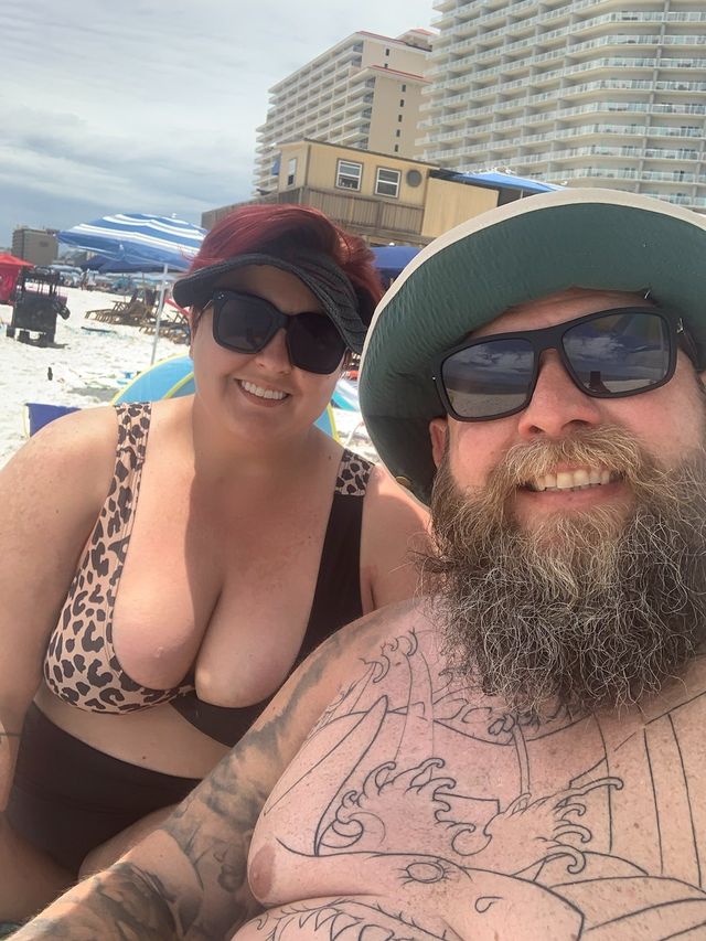Mike and Rachelle selfie. Rachelle wears a lepard print top visor and sun glasses. Mike has the outline of his torso tattoo and wears sun glasses and a gilly hat with the bill flipped up.
