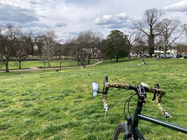 Bicycle handlebars are in the foreground with a park in the background.