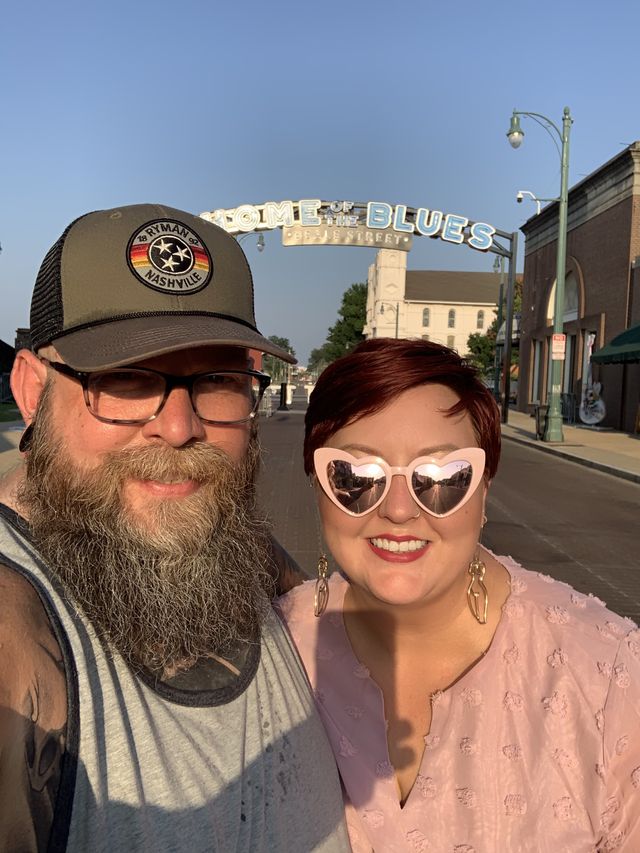 Mike and Rachelle selfie with the bright, late afternoon sun shining directly on them with the Beale Street home of the blues street sign in the background. Rachelle is wearing pink heart glasses.