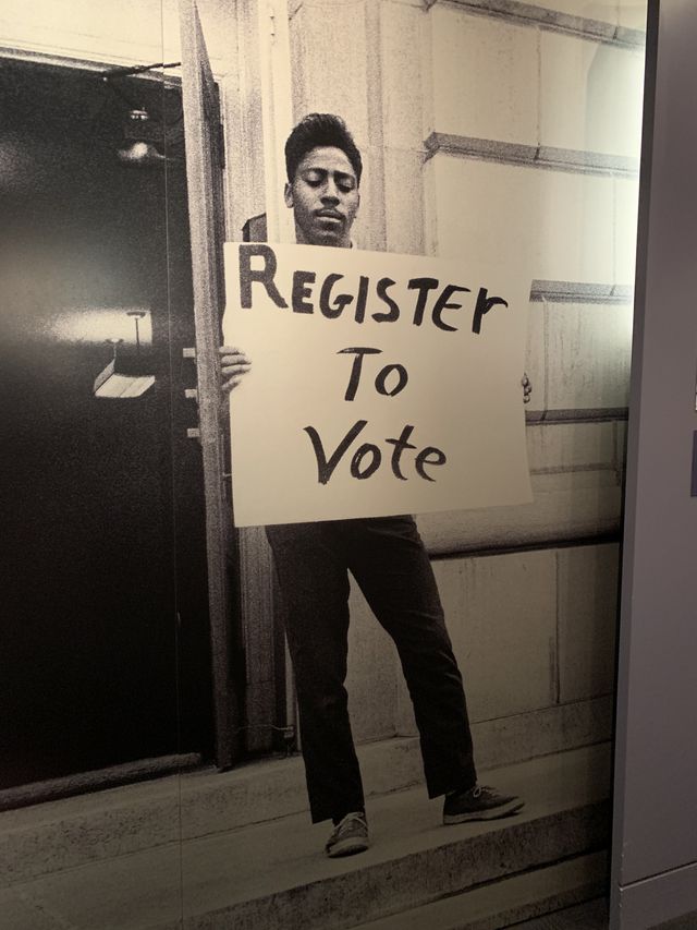 Black and white photo of an African American holding a large sign that says register to vote.